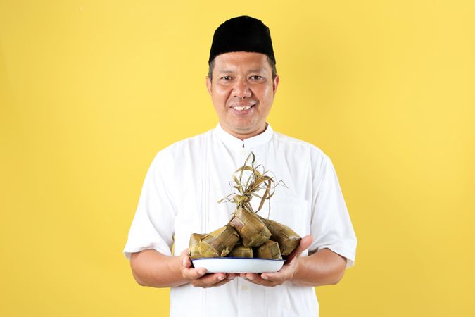 Mature Asian Man Holding A Plat eof Ketupat Rice Cake for Lebaran Ied Al Fitr