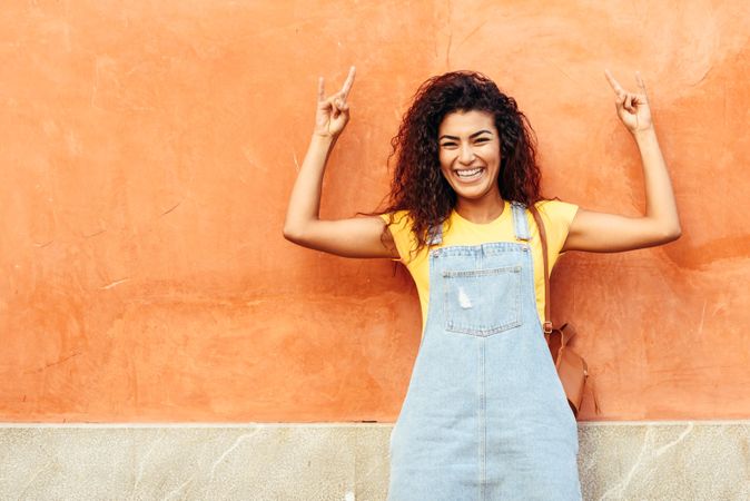 Arab woman with curly hairstyle with arms up leaning on orange wall