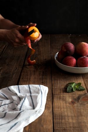 Tasty ripe peaches in plate and hands peeling peach