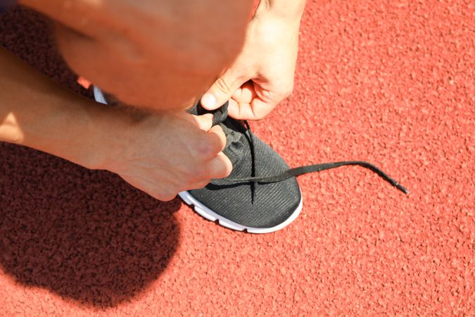 Man tying shoelaces on red athletic running track, close up
