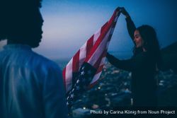 A smiling woman unfolding the American flag at dusk with friend v5qkob
