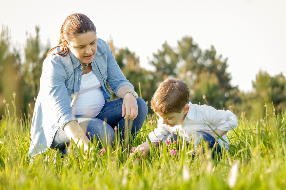 Pregnant mother and son picking flowers in a field