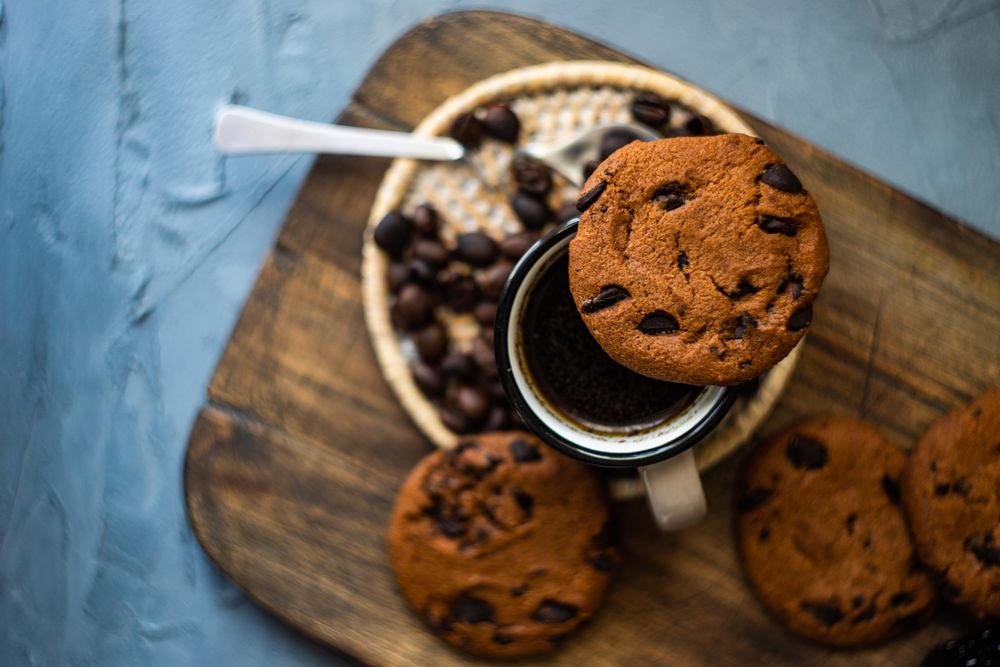Top view of coffee surrounded by cookies on breadboard