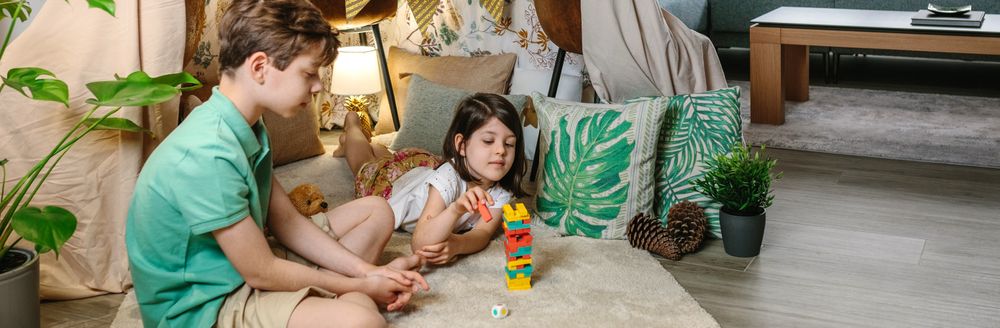 Banner of little girl catching wooden piece of stacking game while play with her brother living room