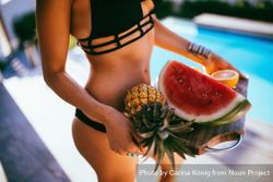 Woman in a bikini holding a fruit platter by the pool B5a3Qb