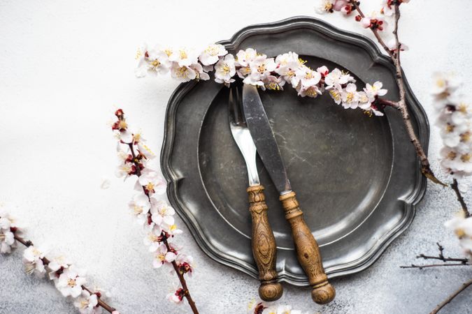 Table setting with delicate apricot blossom around elegant dark tableware on grey counter