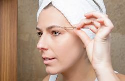 Portrait of woman plucking eyebrows with tweezers