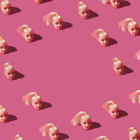 Pattern made of doll heads on pink background