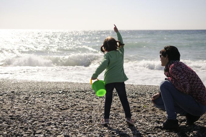 Girl throwing rocks at beach with mother
