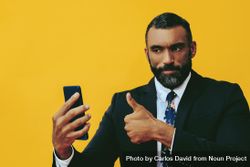 Serious Black businessman in suit giving thumbs up at smartphone screen 0VkGr5