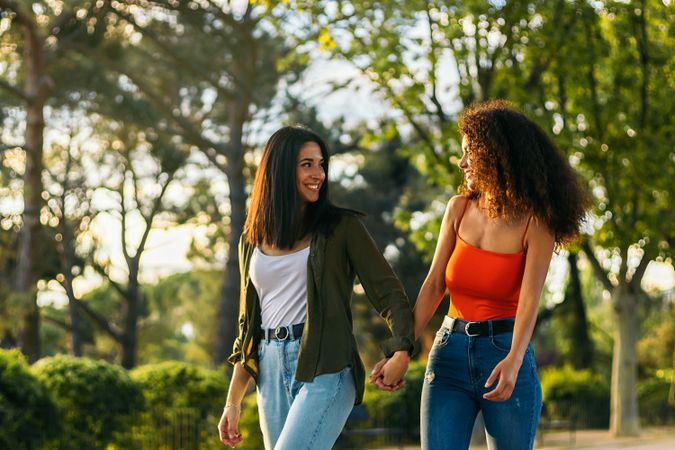 two young women walking holding hands in a park