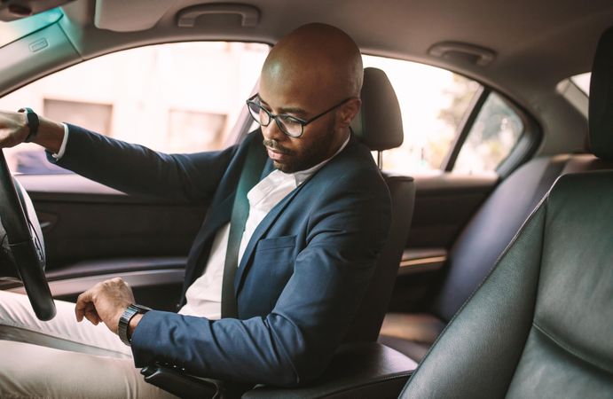 Young Black businessman driving a car and checking time