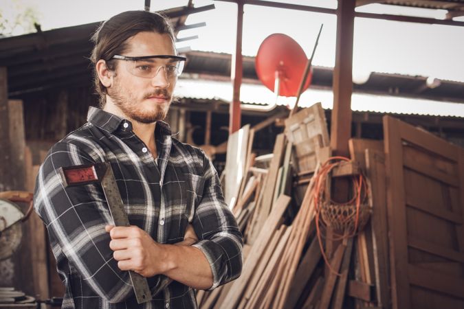 Portrait of male carpenter wearing safety glasses and holding woodworking tool in workshop