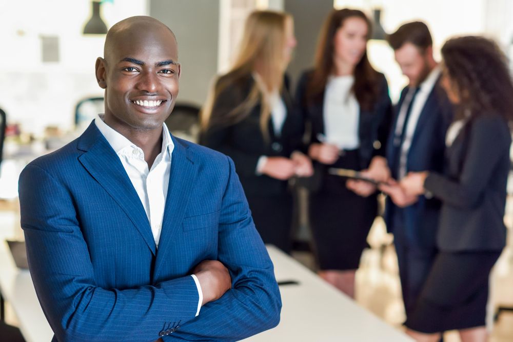 Black male business leader standing in foreground of busy office