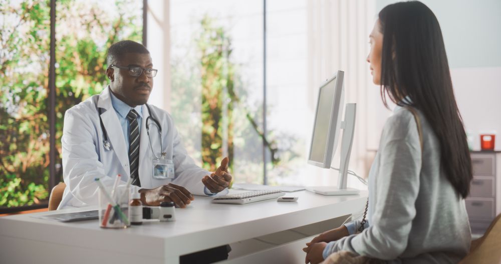 Black Physician in Glasses Prescribing Medicine for a Female Patient and Listening to Her Feedback During Consultation in a Health Clinic.