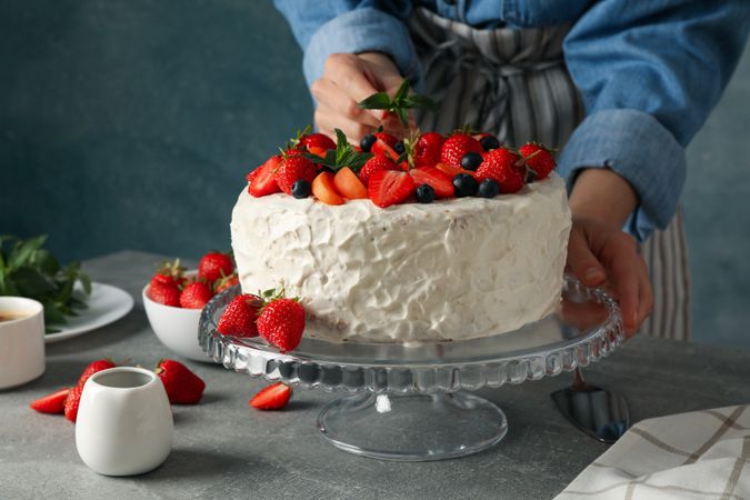 Woman puts mint on berry cream cake. Delicious dessert