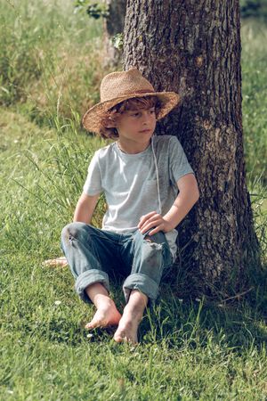 Thoughtful boy relaxing on grass near tree