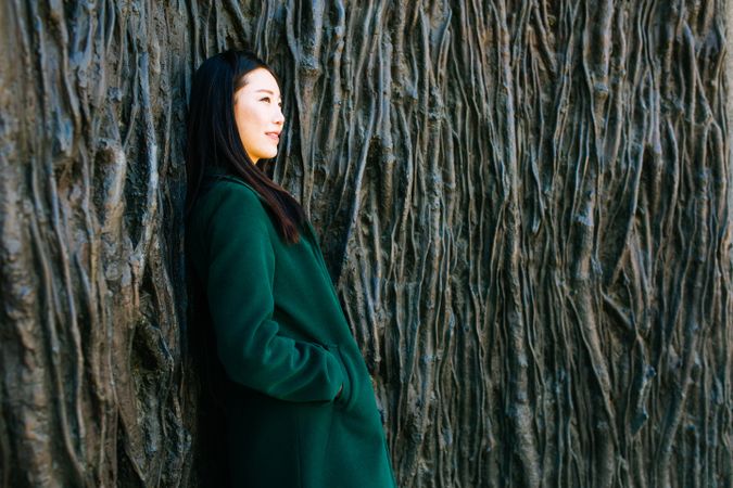 Pensive Asian woman leaning on rough wall