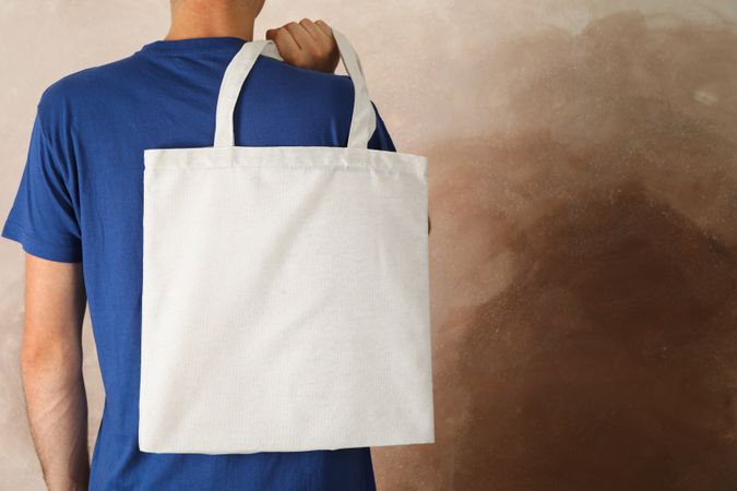 Young man holding tote bag against brown background, empty space