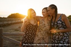 Women in summer dresses hanging out together leaning on wooden fence on coast at magic hour 4BWWxb
