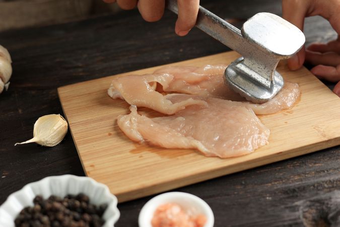 Hands of cook tenderizing chicken breast