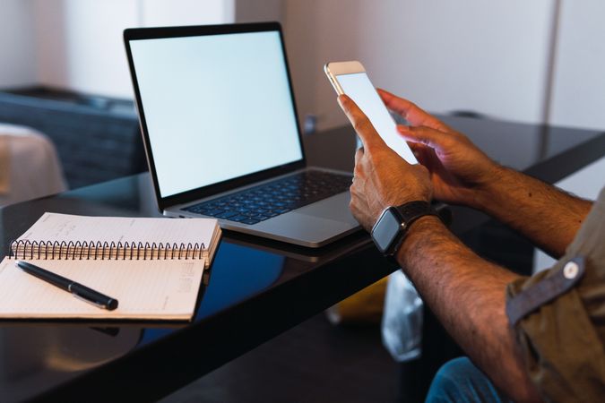 Anonymous man browsing smartphone near laptop