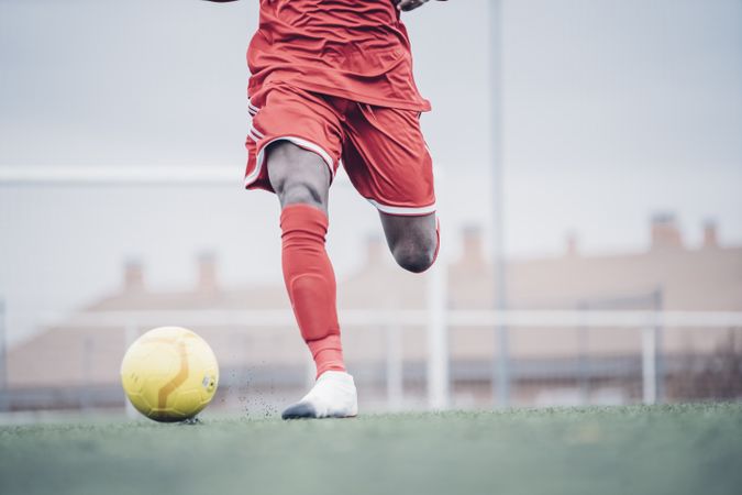 Black soccer player with red outfit playing soccer.