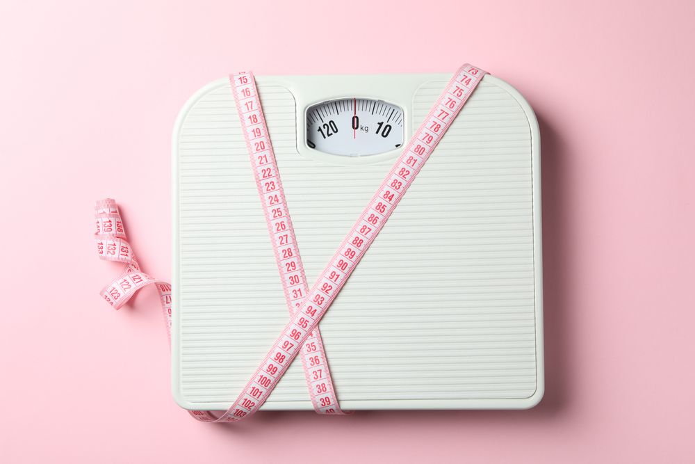 Scales and measuring tape on pink background. Weight loss concept