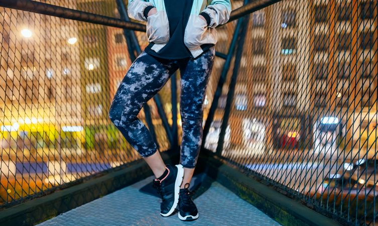 Unrecognizable female runner wearing sporty leggings and sneakers standing on bridge at night
