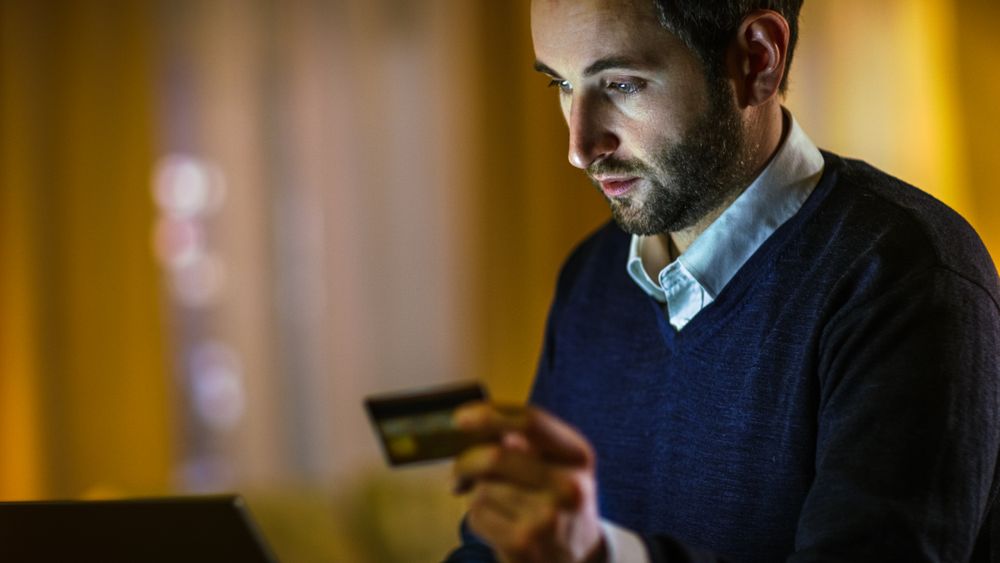 Close-up of a Man at Home He Holds Credit Card and Types It's Number into His Laptop.