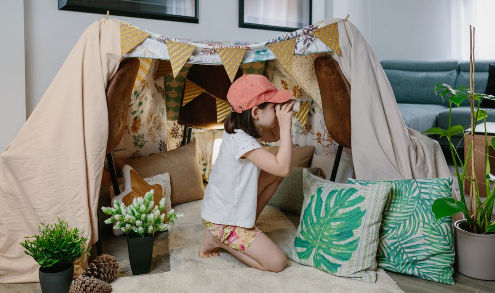 Girl playing with cardboard binoculars while camping at home