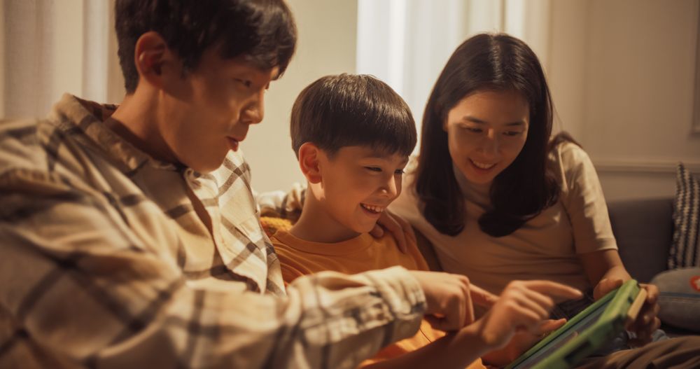 Beautiful Family of Three Using Digital Tablet Computer while Sitting on the Sofa.