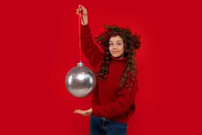 Teen girl wearing Christmas berry wreath holding giant silver ornament.