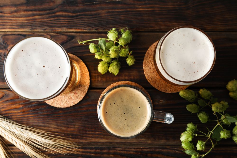 Mugs with beer and hop cones on wooden table, top view