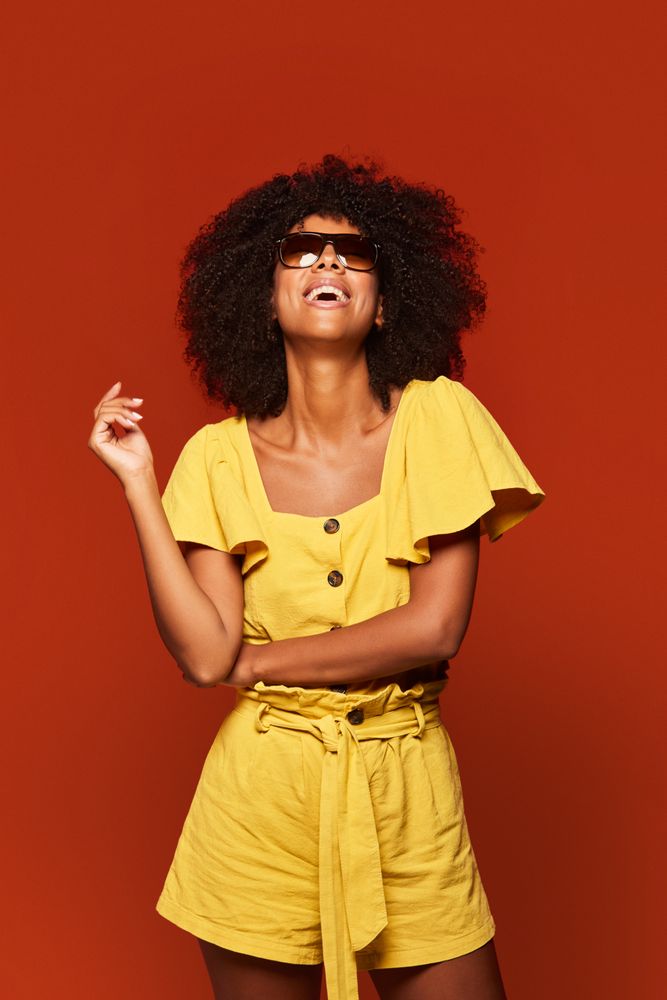 Bright Black woman with hands behind head smiling at camera
