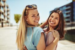 Two female friends looking back and smiling along the river on a sunny day, close up