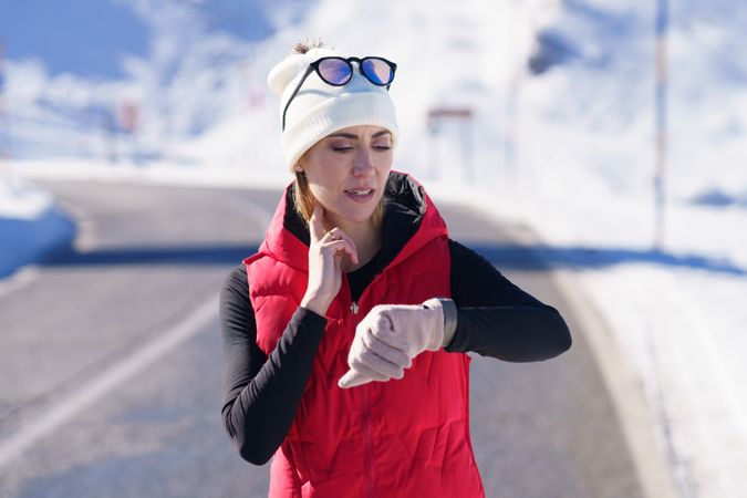 Fit woman in wintry gear checking heart rate while exercising on cold day