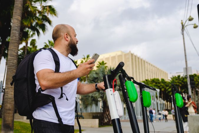 Traveler with backpack browsing smartphone and choosing electronic scooter
