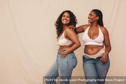 Two women smiling and having fun in studio wearing denim jeans and bras 4BDEX0