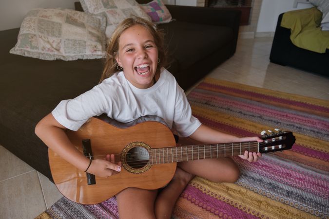 Girl sitting on the floor of a house playing a guitar and singing