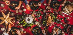 Group of people holding drinks and fork at festive red table with cake, roast chicken, decorations