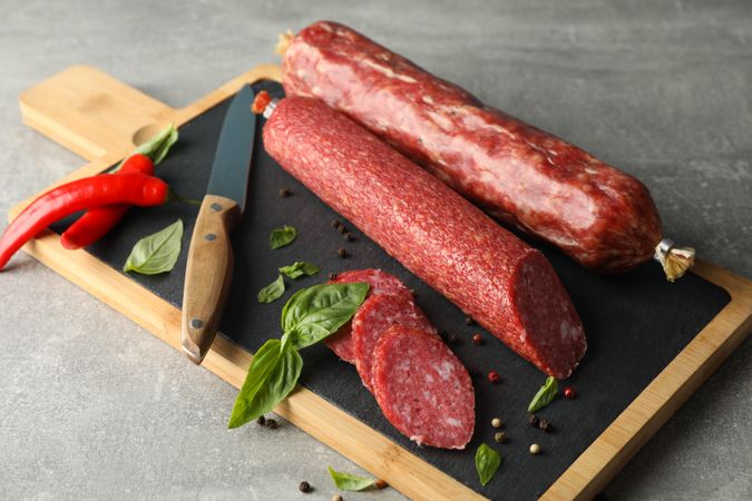 Two sticks of cured meats with slices on wooden board