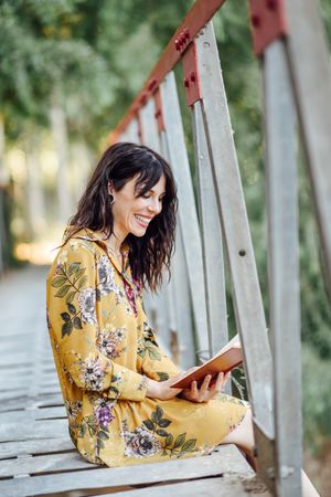 Happy female sitting on a rural bridge and reading