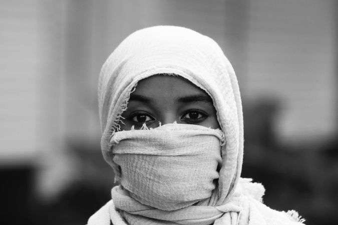 Grayscale photo of young woman wearing headdress hiding her face