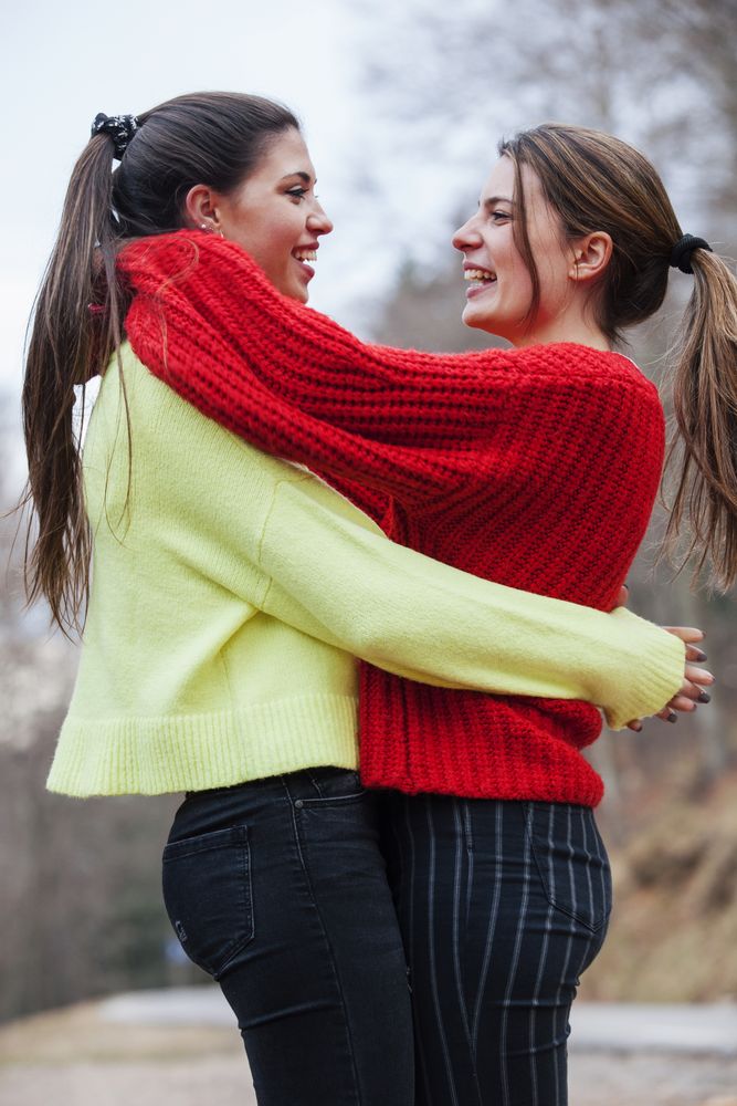 Smiling women in sweaters hugging in park
