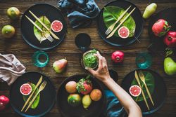 Fresh table setting with leaves on dark plates, fruit with person reaching for pitcher