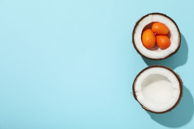 Two half of coconut and whole kumquat on blue background, space for text