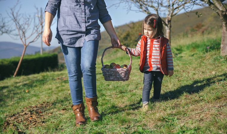 Child and woman carrying basket with apples