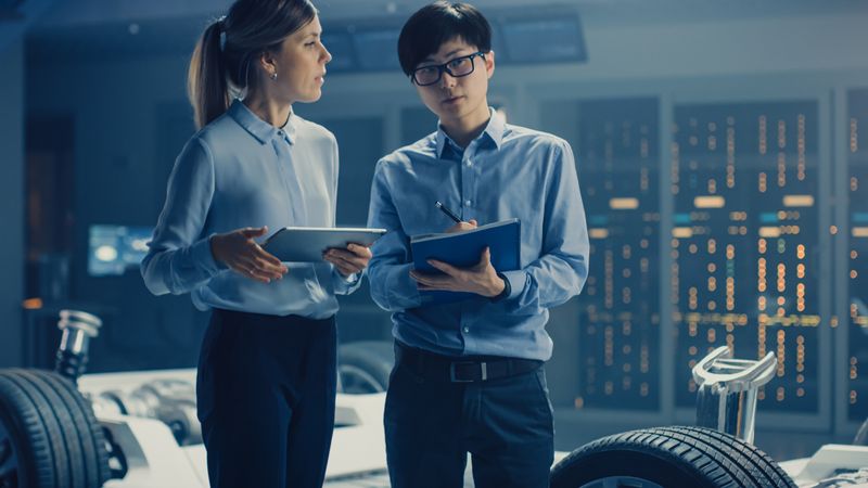 Male and Female Automobile Design Electric Car Engineers Having Conversation, Use Clipboard to Check Maintenance Issues.