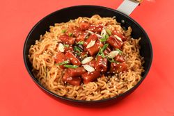 Pan of noodles topped with Korean rice cakes with red background